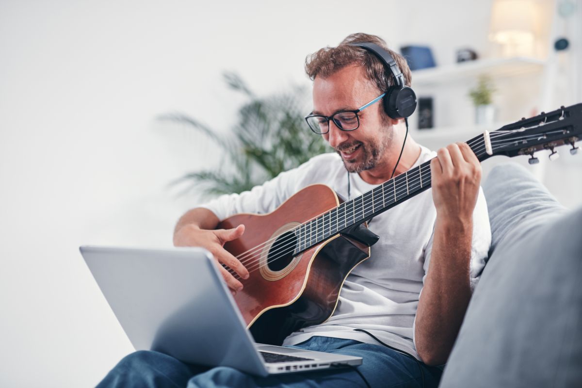 An adult male taking online Guitar Lessons on his laptop